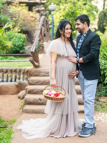 A classic maternity pose on a bridge, with the mom-to-be holding a flower basket, looking lovingly at her partner.