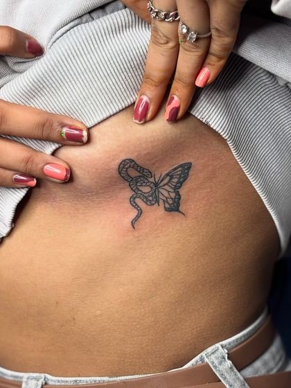 A closer view of the butterfly and snake rib tattoo, showing the fine-line detail in the wings and scales.