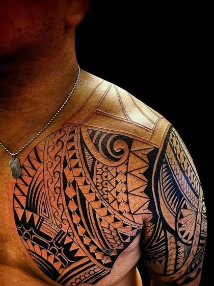 A close-up of a Polynesian tattoo, showing the detailed line work and shading on the shoulder and chest. Each section has a unique pattern that connects to the overall design.