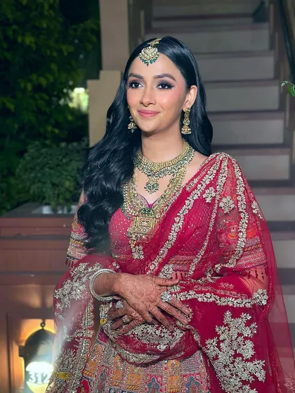 The complete bridal look, showcasing the elegant makeup with the stunning red lehenga and intricate jewelry. The soft glam enhances her features, creating a look that is both radiant and effortlessly chic.