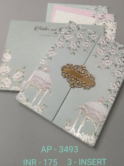A lovely gate-fold invitation in a soft mint green, featuring white floral prints and silver foil accents. An ornate wooden clasp holds the card together, revealing three inserts inside.