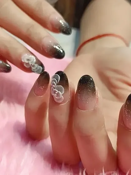 A dramatic black ombré set with a glitter fade, enhanced with delicate 3D white flowers for a touch of elegance.