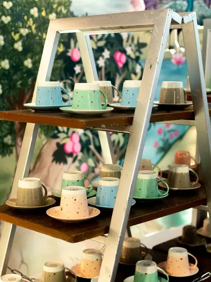 A charming display of colourful, speckled tea cups on a rustic ladder shelf. This is part of our high-tea setup, adding a whimsical and artistic touch to the beverage service.