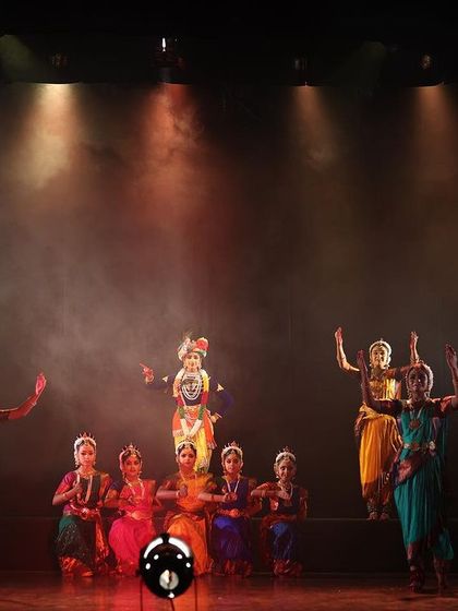 The full stage during a performance of "KRISHNA" at "Nrithya Milanam 2023". This wide shot shows the entire ensemble in a grand, climactic formation.