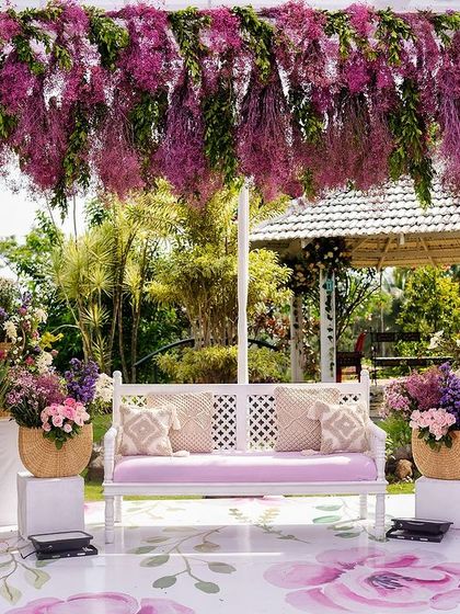 A lovely photo spot with a white bench set under a floral arch bursting with hanging purple flowers, all set on a custom-printed floral floor.