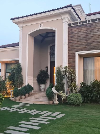 Where textures meet timeless design. This facade blends classic aesthetics like a grand arched entrance with contrasting materials like rustic wood-look tiles, all framed by lush greenery.