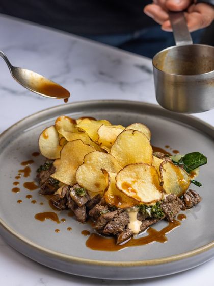 The final touch. A rich jus is poured over our Steak and Frites, bringing together the grilled steak and truffle potato crisps.