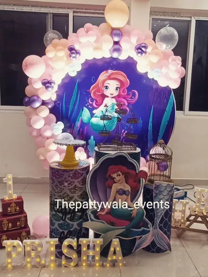 A sweet mermaid theme for a first birthday. The setup includes a large backdrop, themed pedestals, and a light-up name sign.