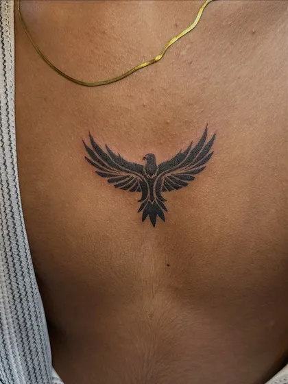 A bold, solid black tribal-style bird tattoo on the back. This minimalist design uses negative space and strong shapes to create a powerful symbol of freedom.
