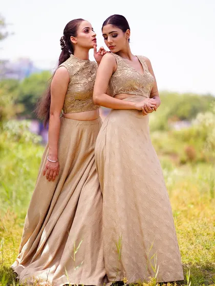 Two models posing together in elegant beige outfits in a sunlit field. Their graceful poses and the natural setting combine to create a soft, romantic, and high-fashion image.