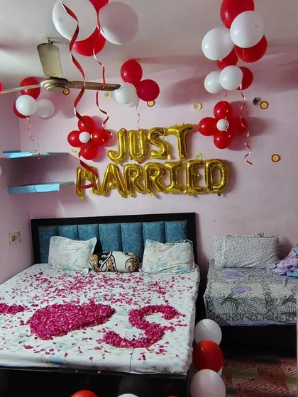 A simple and sweet 'Just Married' room decoration. The bed is covered in rose petals spelling 'I Love You', and the room is filled with red and white balloons to celebrate the new beginning.