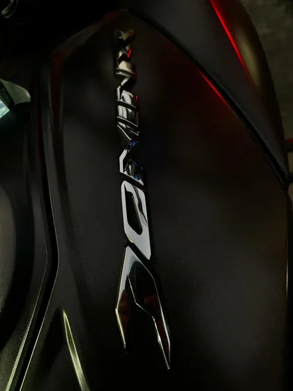 A close-up, artistic shot of the Dominar logo on the fuel tank, captured in the ambient light of city traffic.