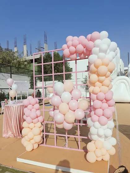 A simple yet chic outdoor setup featuring a pink grid wall decorated with a pastel balloon garland. This modern and minimalist approach is perfect for a stylish baby shower or birthday party.