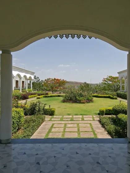 A view from a covered veranda at the National Judicial Academy frames the meticulously maintained gardens. The design uses traditional architectural elements like arches to create a seamless transition between indoor and outdoor spaces.