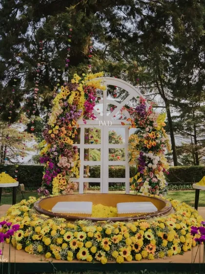 The central seating area for the Haldi, framed by a beautiful floral arch. The combination of yellow and purple created a stunning visual against the green landscape.