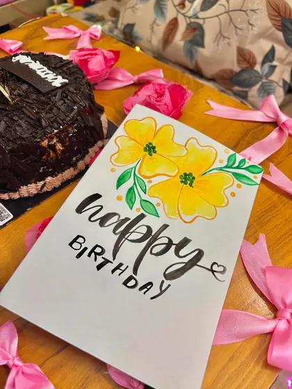 The birthday card pictured with a chocolate cake and pink ribbons.