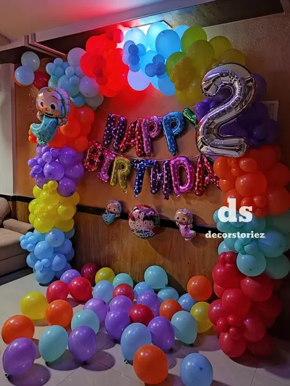 A bright and cheerful Cocomelon theme for a second birthday. The decoration includes a vibrant, multi-colored balloon arch, character foil balloons, and a large number '2' foil balloon.