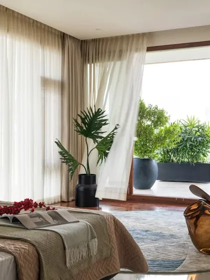 The guest bedroom opens onto a verdant balcony, with sheer curtains diffusing the light to create a soft, breezy atmosphere. The space is designed to feel open and connected to the outdoors.