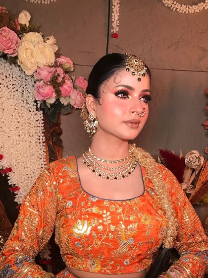 A close-up of the makeup and hairstyle for the orange lehenga look. The hair is styled in a chic, traditional bun with delicate baby hairs.