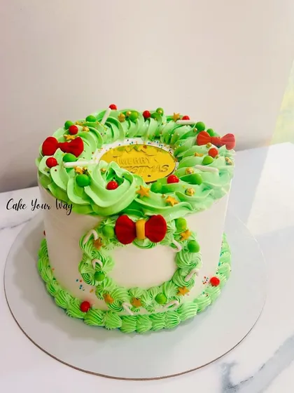 A Christmas wreath cake with festive green piping and red bows.