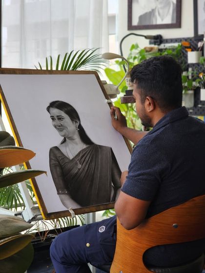 Me at my drawing board working on a portrait of a woman in a saree. My studio is my sanctuary, filled with plants and natural light.