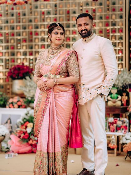 A beautiful portrait of a couple celebrating their baby shower. Her pink Kanchipuram silk saree with a heavily embroidered blouse is perfectly complemented by his custom-designed embroidered bandhgala jacket.