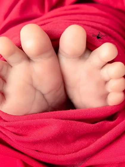 A macro shot of tiny newborn toes peeking out from a cozy red wrap. It’s a classic detail shot that parents always adore.