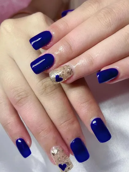 A striking set of royal blue square nails with a gold glitter accent nail featuring a small blue heart.