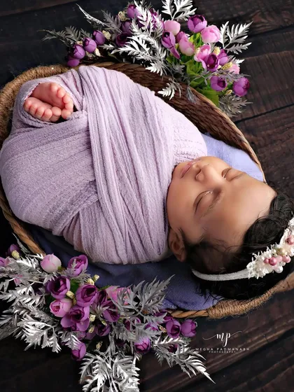 A beautiful composition with a baby in a lavender wrap, surrounded by purple and silver flowers in a dark-toned basket.