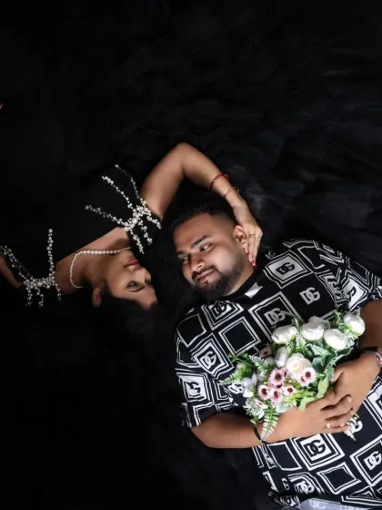 A highly artistic and modern top-down portrait. The couple lies on a black background, creating a striking, graphic composition that feels both intimate and stylish.