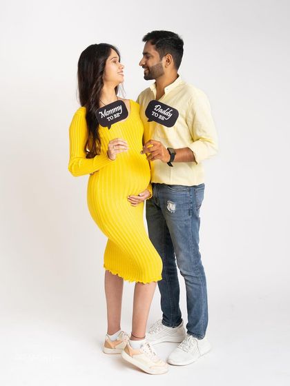 A playful and modern portrait of the parents-to-be. Dressed in bright yellow, they look at each other while holding "Mommy to be" and "Daddy to be" signs.