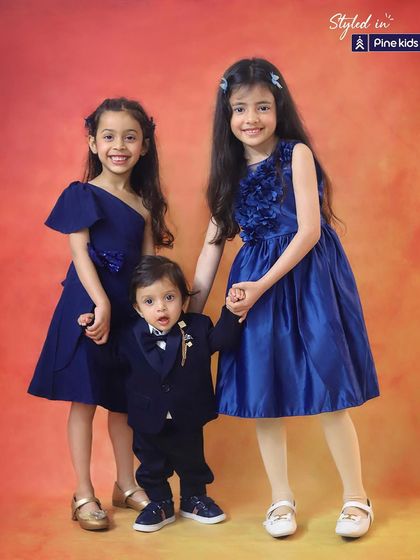 A trio of stylish siblings! This studio portrait showcases the bond between two sisters and their dapper little brother, all dressed in beautiful blue outfits.