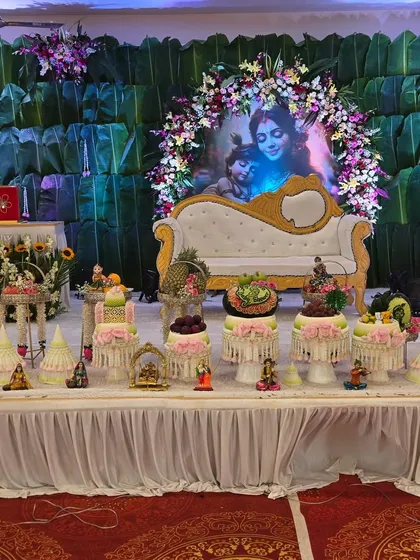A stunning, full-stage setup for a Krishna-themed `dohale jevan`, complete with a floral arch, traditional fruit displays, and our food tables.