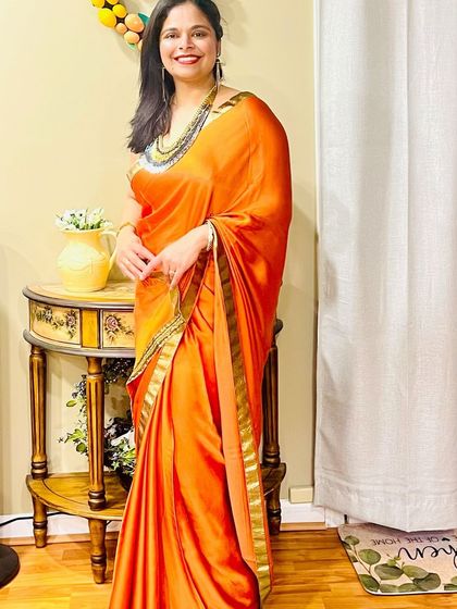 A client looking radiant in a vibrant orange saree. She styled it with a long, multi-layered traditional necklace that adds a touch of heritage and grace to her look.