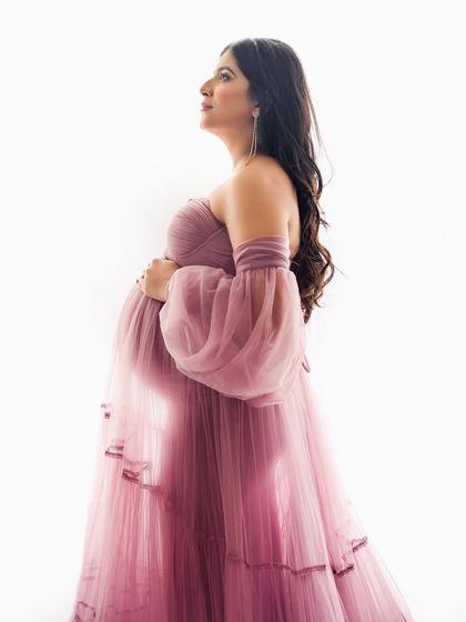 A silhouette of pure elegance. This portrait uses backlighting to highlight the sheer fabric of the gown and the beautiful shape of the baby bump, creating a soft and artistic effect.
