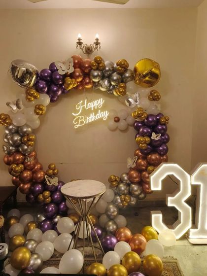 A chic 31st birthday party at home. This setup features a circular balloon arch in purple, gold, and silver, a neon sign, and large '31' marquee numbers.