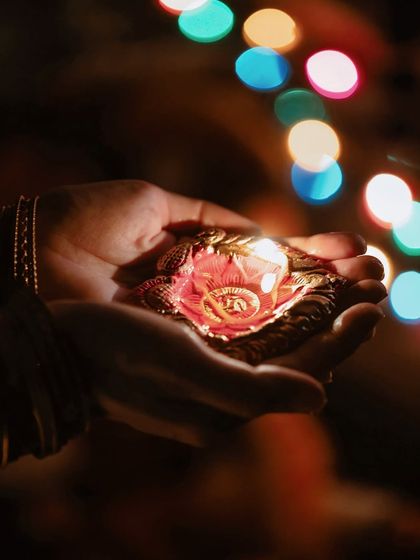 A close-up on hands holding a beautifully decorated diya, with colorful bokeh lights in the background, symbolizing the offering of light during the festival.