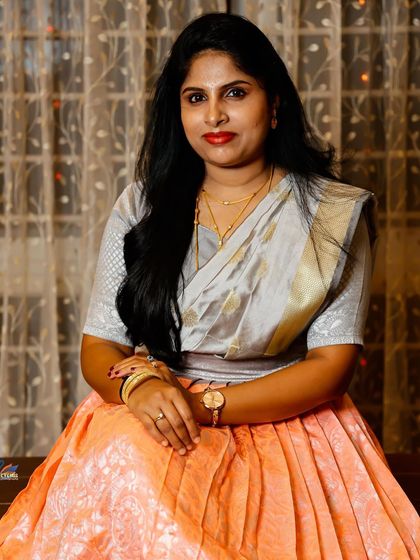 A simple and elegant portrait of a woman in a traditional half saree, seated in a warmly lit room.