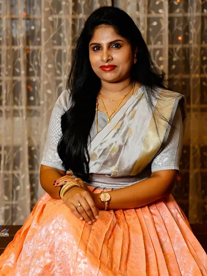 A simple and elegant portrait of a woman in a traditional half saree, seated in a warmly lit room.