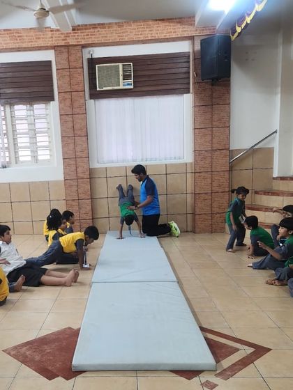 A coach carefully spots a young student during a gymnastics drill. Safety and proper technique are paramount as we introduce children to new physical challenges.