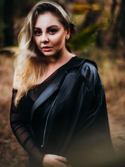 A portrait from a photoshoot in a natural, wooded setting. The leather jacket and dark clothing create a cool contrast with the organic background.