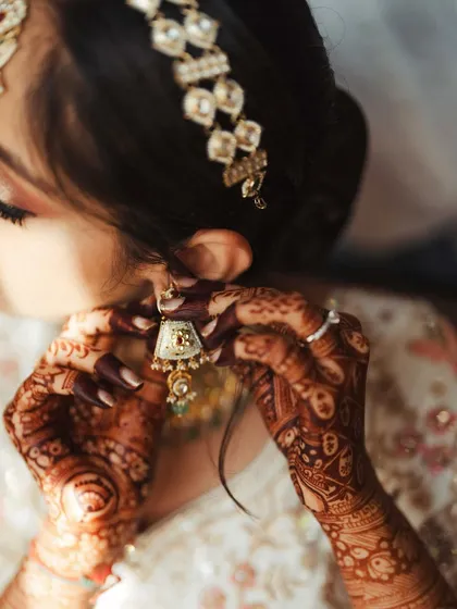 A detailed shot of the bride putting on her earring, her mehendi-covered hands adding to the beauty of the frame.