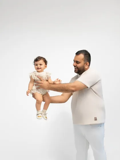 A father holds his daughter, both smiling happily. The clean, minimalist background ensures their bond is the central focus of the image.