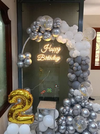 A chic grey, silver, and white balloon arch for a 2nd birthday. This modern and minimalist setup includes a 'Happy Birthday' neon sign and a large gold foil number '2'.