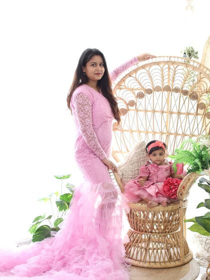 A full-length portrait of a mother and daughter in matching pink outfits. The little one sits in a peacock chair, creating a sweet and stylish "mommy and me" photo.