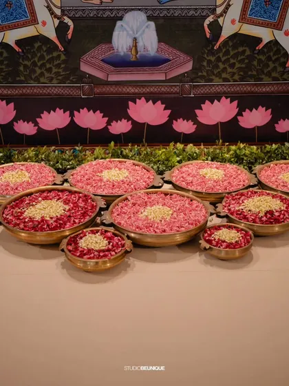 Brass bowls filled with rose petals and jasmine, set against a Pichwai-style backdrop. This is a beautiful way to incorporate traditional art and fragrances.