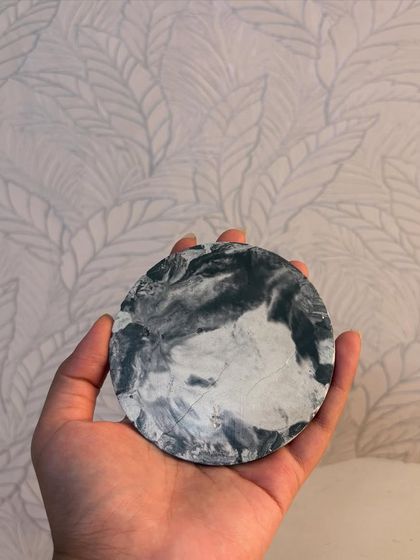 Holding the round ceramic coaster to show its handmade quality and the unique, one-of-a-kind marble pattern on its surface.