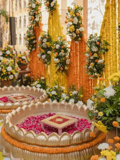A close-up of the Haldi ceremony seating, featuring large brass urlis filled with flower petals, set against a backdrop of marigold garlands and fresh floral arrangements.