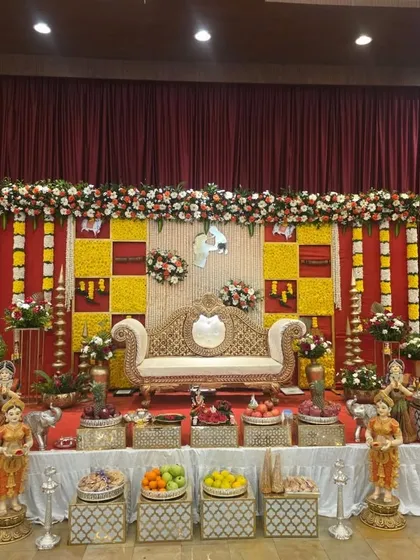 A vibrant stage with a backdrop of red and yellow checkered flower panels. This is a classic South Indian design, perfect for auspicious occasions.