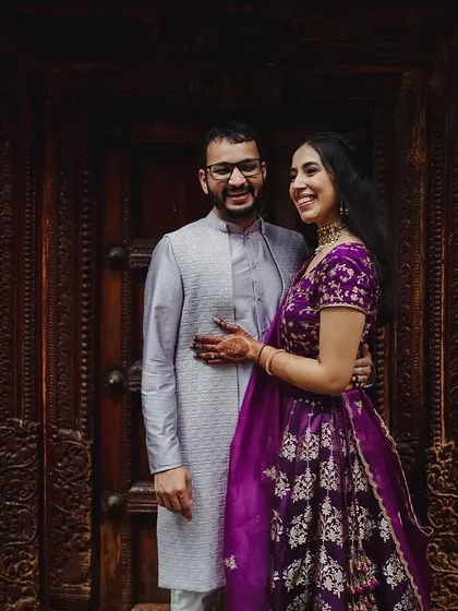 A couple in coordinated outfits stands against a rustic stone and wood door, a perfect blend of modern style and heritage charm.
